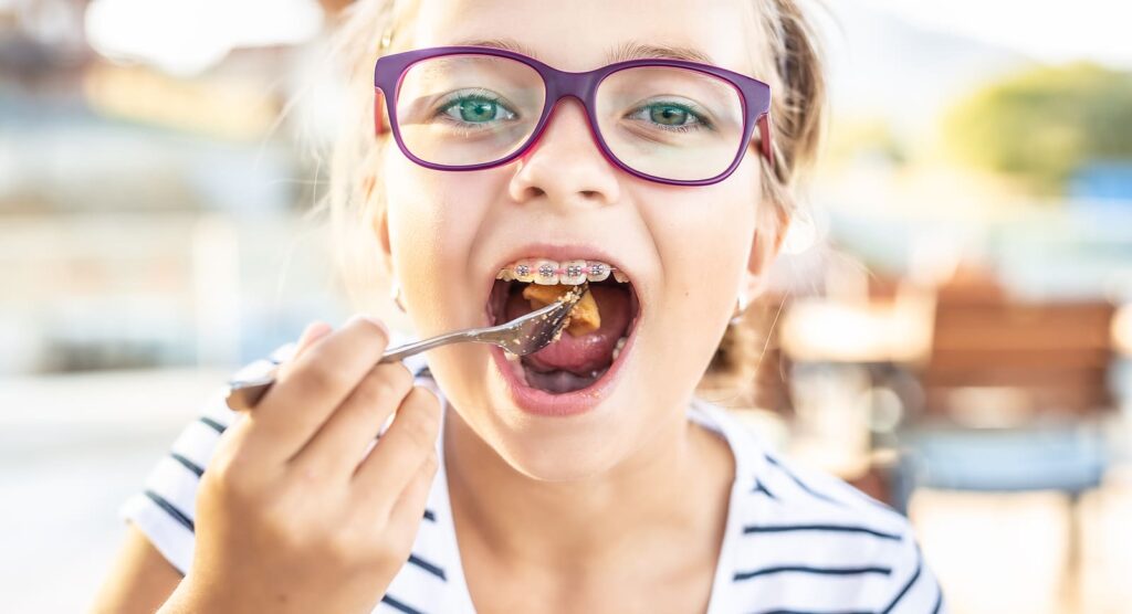 A little girl wearing braces freely enjoying her food
